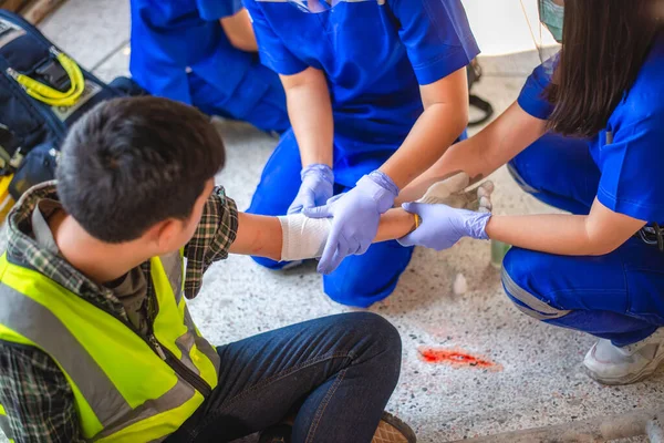 İnşaat işçisinin işyerinde fiziksel yaralanma. Acil sağlık ekipleri ilk olarak inşaat alanında kaza geçiren bir inşaat işçisine yardım ediyor..