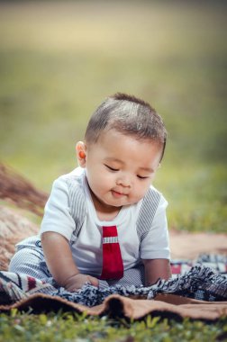 A little boy is sitting on a cloth spread on the grass in the park. 6 month old boy.