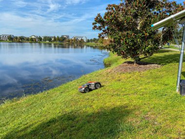 Orlando, FL. / USA - 10 / 16 / 20: Bir Husqvarna otonom çim biçme makinesi Orlando, Florida 'daki Laureate Park mahallesinde bir gölün yakınında biçiyor
