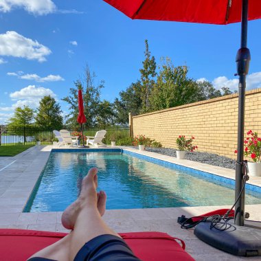 Kırmızı şemsiyeli ve parlak mavi gökyüzü olan rahatlatıcı bir arka bahçe yüzme havuzu..