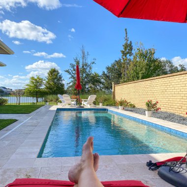 Kırmızı şemsiyeli ve parlak mavi gökyüzü olan rahatlatıcı bir arka bahçe yüzme havuzu..