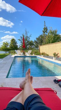 Kırmızı şemsiyeli ve parlak mavi gökyüzü olan rahatlatıcı bir arka bahçe yüzme havuzu..