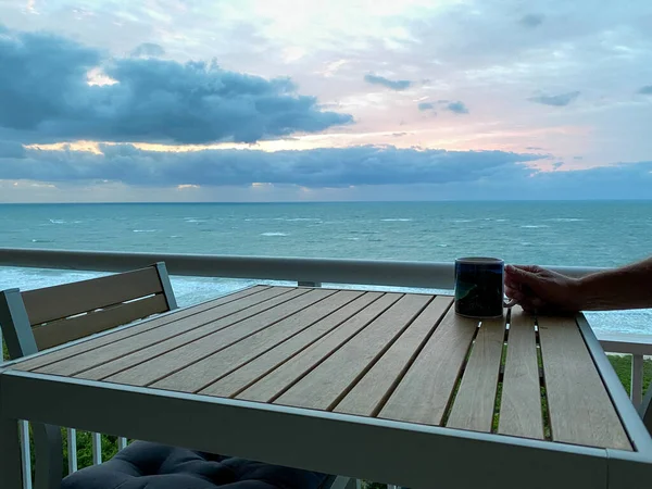 A coffee cup on a table with a vibrant sunrise over the Atlantic Ocean on North Hutchinson Island in Florida in the background.