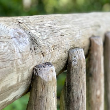 Botanik bahçesindeki köprüden gelen gri ahşap bir tırabzanın makrosu. Arka plan olarak kullanılabilecek bir bulanıklık var..