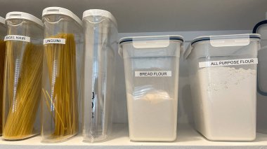 Plastik kaplarda çeşitli makarna ve un çeşitleriyle organize bir kiler rafı..