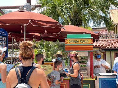 Orlando, FL USA - 2 Mayıs 2021: İnsanlar Disney World Magic Kingdom 'daki bir yemek arabasından Cheeseburger ve Pepperoni Spring Rolls almak için sırada bekliyorlar.