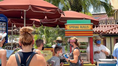 Orlando, FL USA - 2 Mayıs 2021: İnsanlar Disney World Magic Kingdom 'daki bir yemek arabasından Cheeseburger ve Pepperoni Spring Rolls almak için sırada bekliyorlar.