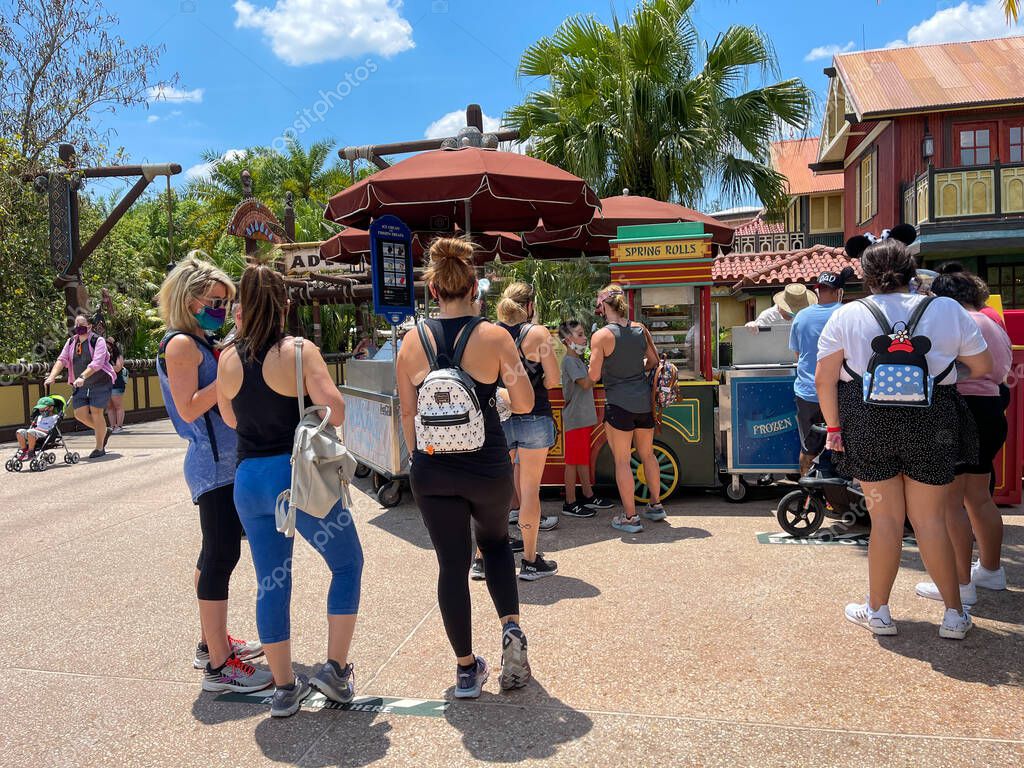 Orlando, FL USA - May 2, 2021:  People waiting in line to buy Cheeseburger and Pepperoni Spring Rolls from a food cart at Disney World Magic Kingdom.