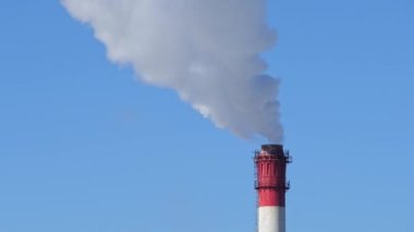 Mavi gökyüzündeki elektrik santrali bacası. Kırmızı tüpten beyaz buhar..