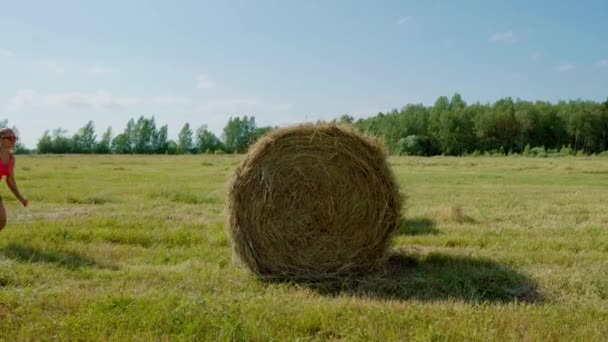 Elegantní dívka v létě v poli se snaží skočit na kupku sena — Stock video