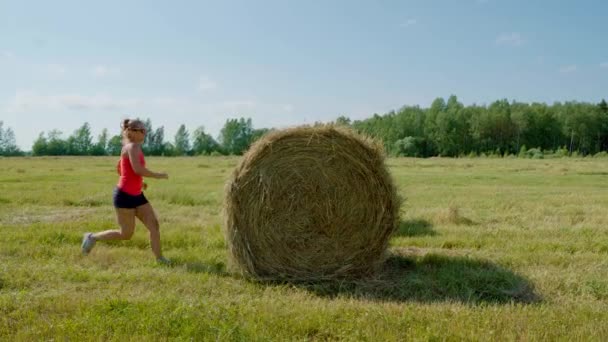 Элегантная девушка летом в поле пытается прыгнуть на стоге сена — стоковое видео