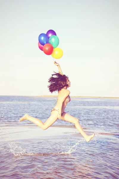 Beautiful and athletic brunette girl with colorful balloons jump — Stock Photo, Image