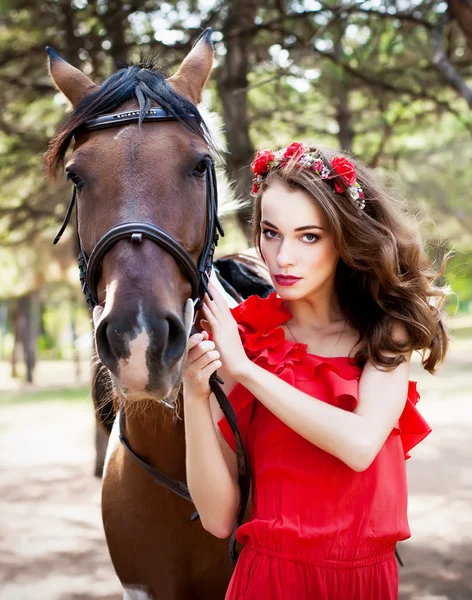 Bella giovane signora che indossa abito rosso cavalcando un cavallo a sole s — Foto Stock