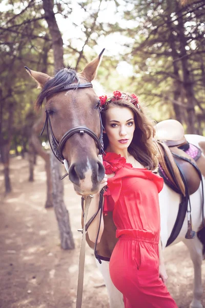 Барышня в красном платье верхом на лошади на солнечных лучах — стоковое фото