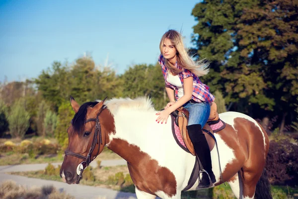 Schöne junge Frau in T-Shirt und Jeans beim Reiten auf einem Pferd — Stockfoto