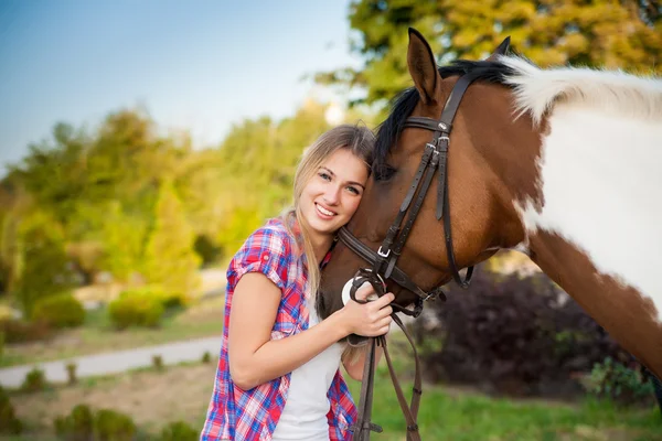 Schöne junge Frau in T-Shirt und Jeans, die an einem sonnigen Sommertag auf einem Pferd reitet. blondes langes Haar mit einem glücklichen Lächeln. perfekte Haut und Make-up. Nahaufnahme. Außenschuss. — Stockfoto