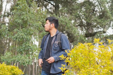 Ormanda yürüyen genç adam. Sırt çantası, cep telefonu kaydı ve fotoğraf çekerek..