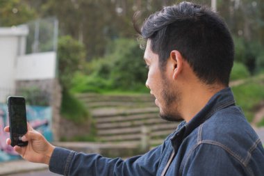 Ormanda yürüyen genç adam. Sırt çantası, cep telefonu kaydı ve fotoğraf çekerek..