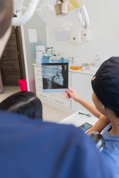年轻的女牙医检查病人的X光片 教你要做的整个牙科手术 — 图库照片