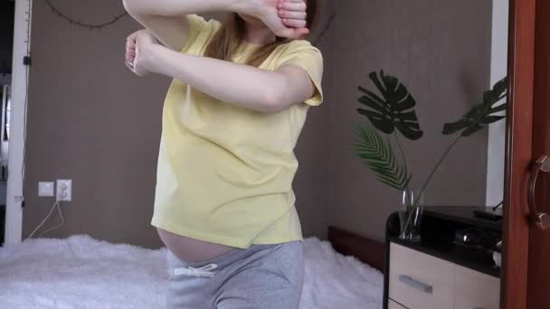 黄色のTシャツのダンスで腹を持つ妊娠中の女の子は 修道院の観葉植物を背景に自宅で喜びます 母性は喜びです 幸せな妊娠 — ストック動画