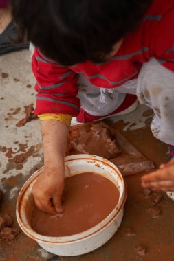 Çocuk parmaklarıyla çamurdan bir parça alıyor. Kil figürleri modelleniyor