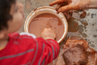 Çocuk, küflenmek için elini balçığa daldırıyor. Kil figürleri modelleniyor