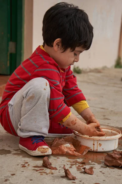 Diz çökmüş ve çok konsantre olmuş bir çocuk kilden şekiller yapar..