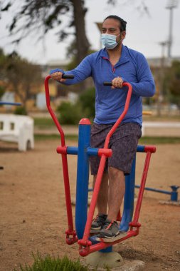 Maskeli adam halka açık meydanda makineler üzerinde eliptik egzersizler yapıyor. yeni normal. spor oturumu