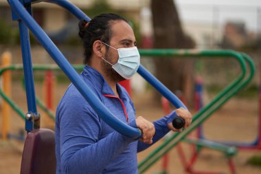 Mavi tişörtlü adam halka açık parkta vücut ağırlığı egzersizi yapıyor. Yan atış. Spor seansı. covid oturumu