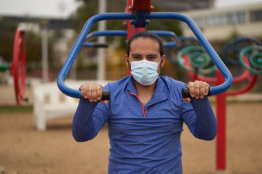 Mavi tişörtlü bir adam halka açık bir parkta vücut ağırlığı egzersizi yapıyor. Spor seansı. covid oturumu