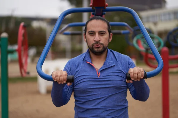 Mavi tişörtlü adam halka açık parkta vücut ağırlığı egzersizi yapıyor. Spor oturumu