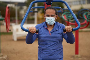 Yeni normal. Adam, yüz maskesi, çene bağı ve spor kıyafetleriyle şınav çekiyor. Parkta egzersiz yapan bir adam. Spor oturumu