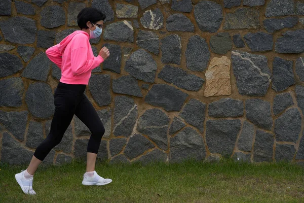 Maskeli kadın çimenlerde koşar. Yeni normal. Spor oturumu