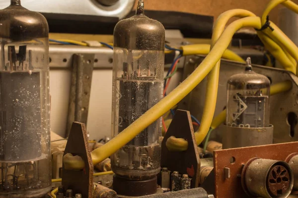 Electron tubes in an old, dusty radio. In the background electronic parts and colored electric wires.