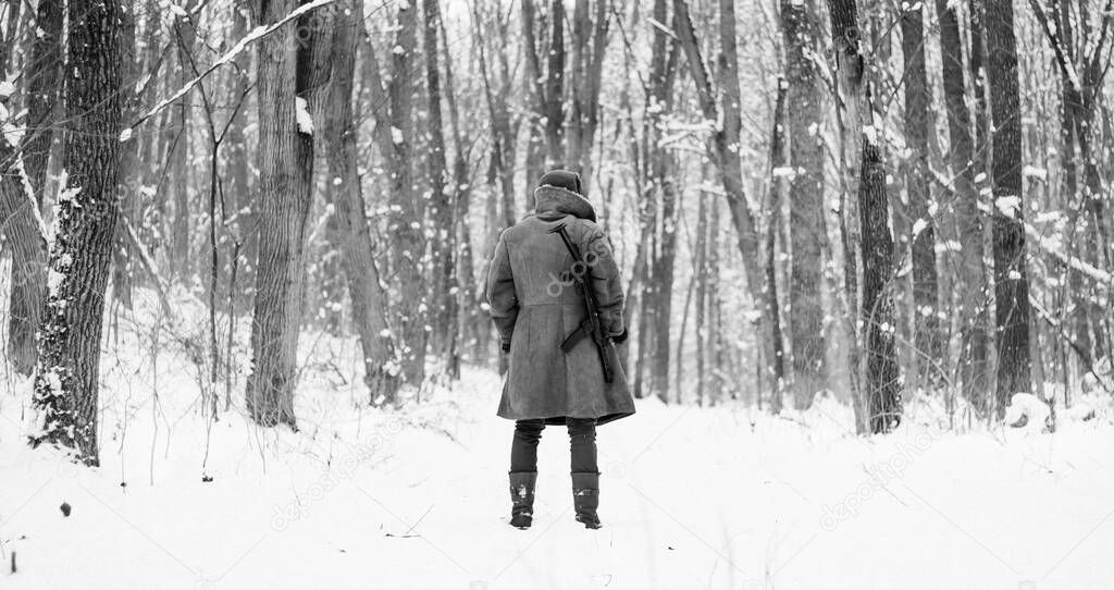 Soviet soldier in coat is standing with a gun in the winter forest 