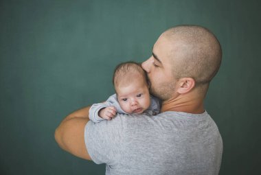 Kısa saçlı genç baba yeni doğmuş kızını öpüyor.
