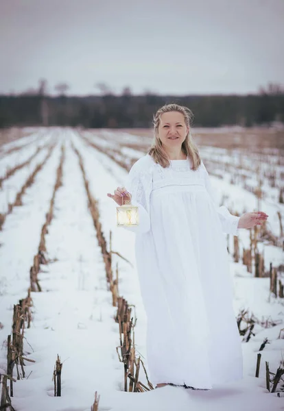 Attractive woman in nightgown in the field in winter with hand lamp