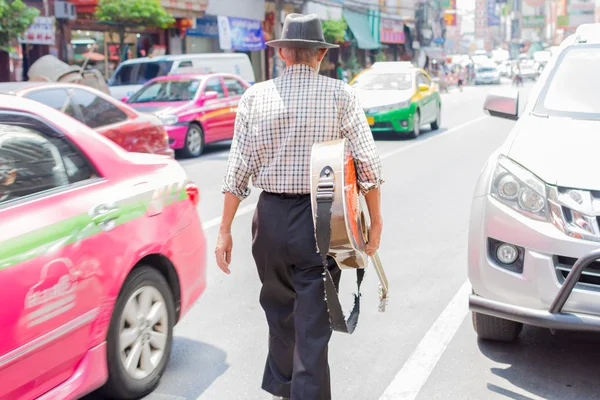 Παλιά ο άνθρωπος περπατώντας στον δρόμο κρατώντας μια κιθάρα. — Φωτογραφία Αρχείου