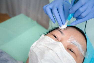 Kaş dövme kliniğinde ya da Kaş nakış kliniğinde çalışan doktor tarafından yapılan Asyalı kadın kaş dövmesi dövmesi. Dövme ve düzeltme için KOVID-19 önleme politikası kullanın.