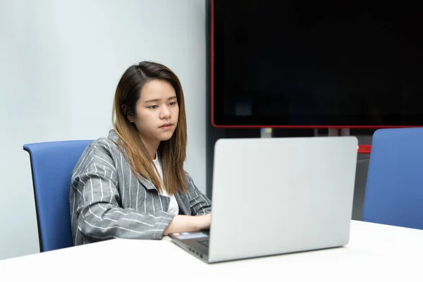 Asian woman is student,businesswoman working by computer notebook, laptop in office meeting room with whiteboard background with annoyed, displeased emotion in concept working woman,unhappy in life