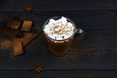 Bir fincan kremalı sıcak çikolata, tarçın ve koyu kahverengi arka planda anason..