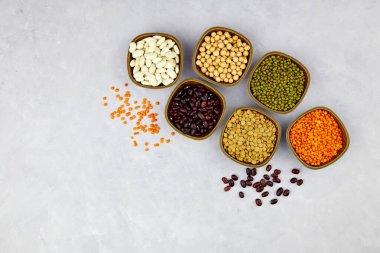 Kaplarda baklagiller ve fasulye çeşitleri: mercimek, fasulye, mung ve nohut hafif taş arka planda. Üst görünüm, boşluğu kopyala. Sağlıklı vejetaryen protein yiyeceği.