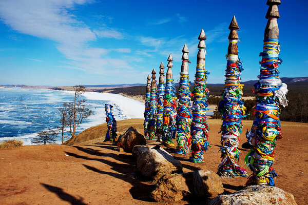 Wooden ritual pillars with colorful ribbons on cape Burhan or Shamanka rock.  Lake Baikal, Olkhon Island in winter.