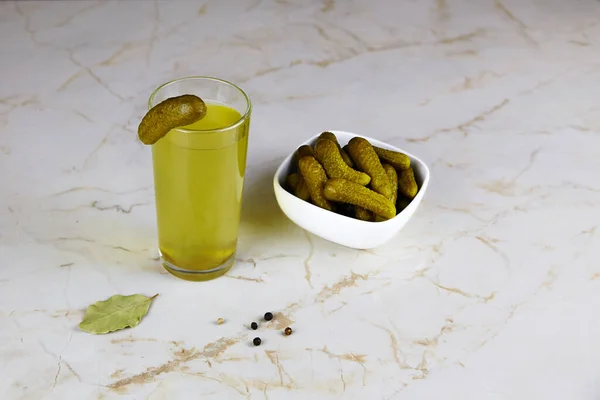 Pickle juice or cucumber pickle in glass and a bowl with pickled cucumbers on on light background. A healthy drink after a sports workout. — Stock Image Pickle Juice Cucumber Pickle Glass Bowl Pickled Cucumbers Light Background Stock Photo