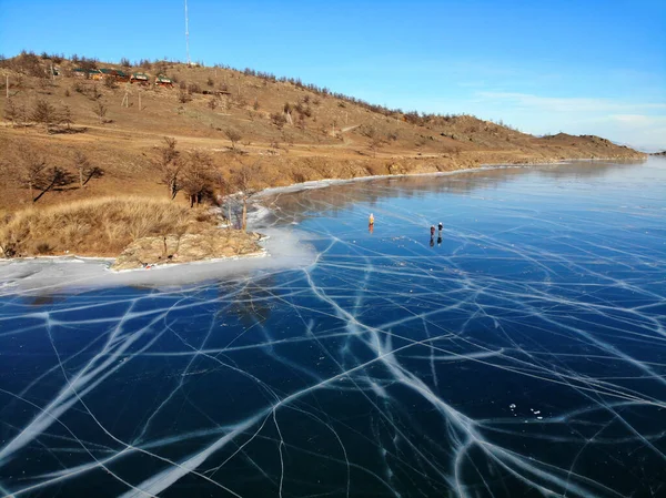 Lake Baikal in winter from the air. Clear transparent ice with Cracks. Tourists walk and skate on the Baikal ice.