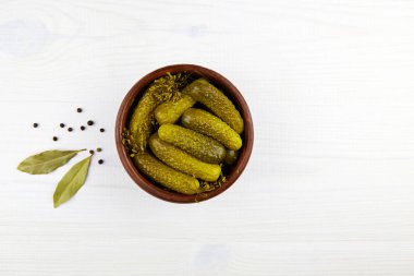 Beyaz ahşap arka planda seramik bir kasede salatalık turşusu. Üst görünüm, alanı kopyala