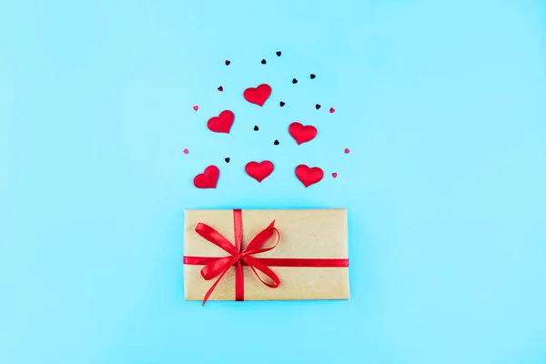 Gift box in a craft paper package with a red ribbon. Hearts, romantic decorations  on a blue background. Valentine\'s Day, Mother\'s Day, Birthday, Christmas.