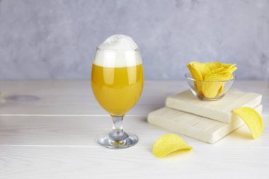 Beyaz ahşap arka planda cipsleri olan bir bardak light bira..