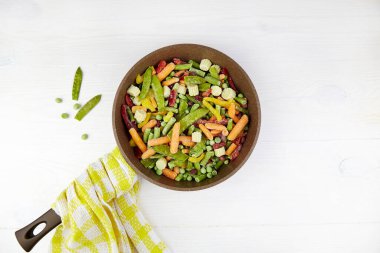 Kızartma tavasında donmuş sebzeler, beyaz ahşap arka planda. Üst görünüm.