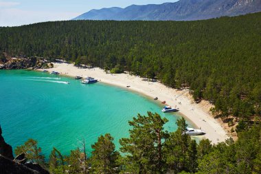 Güneşli yaz gününde güzel kumlu sahil. Baykal Gölü, Sandy Körfezi. Kıyıya yakın yatlar, güneşlenen turistler.